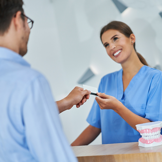 Man handing his credit card to a receptionist at a dental office