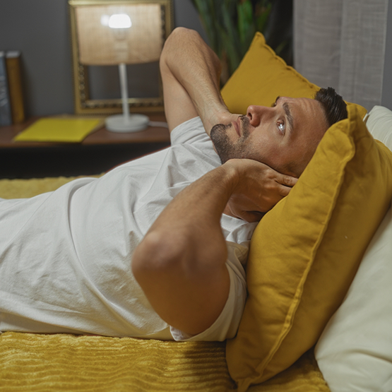 Man laying awake in bed and covering his ears with his hands