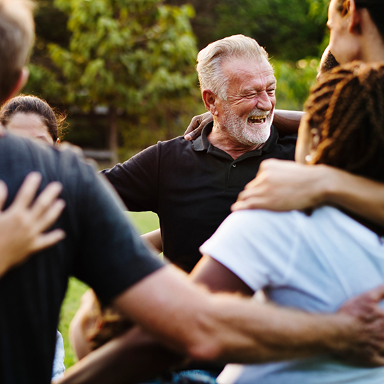 Group of people laughing outdoors with their arms around each other's shoulders