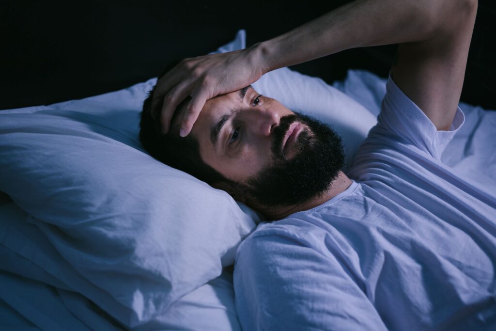 Man awake in bed placing hand on forehead