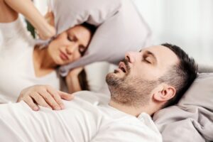 snoring man with sleep apnea and his annoyed partner next to him