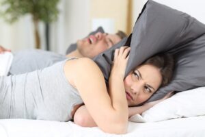 Woman holding pillow over her head while partner snores. 